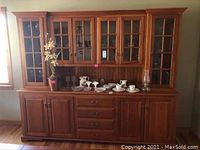 Full front view of large wooden buffet with glass door upper cabinets and drawers in lower section with various decorative items on countertop.