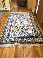 Full view of rug laid on hardwood floor showing overall pattern and fringe.