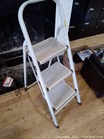 Front view of the white metal 3-step ladder showing all three steps and curved handle.