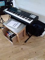 Roland FA-06 keyboard mounted on stand with bench and books underneath, soft case behind