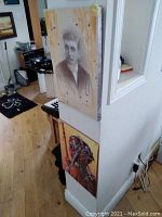 Two prints mounted on a wall corner, one showing a portrait and the other a sci-fi themed figure with a gas mask.