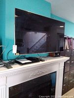 Front view of Samsung flat-panel TV on mantel with Blu-ray player and other devices beneath.