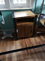 Closed wooden cabinet with metal frame positioned under window, showing front with door labeled '25 EST. 1962 TEXAS'