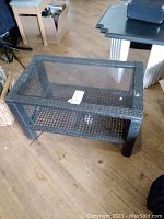 Full view of rectangular faux wicker patio table with glass top showing woven wicker sides and clear glass insert.