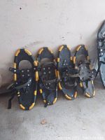 Two pairs (four total) of yellow and black snowshoes leaning against a wall, showing the top side with straps for foot securing.