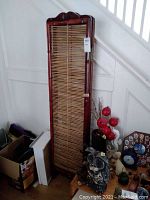 Full view of tall narrow two-panel wooden privacy screen with bamboo slats leaning against white staircase.