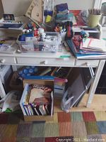 White table with clear plastic containers filled with paints, markers, colored pencils, and brushes along with art books in a box underneath.