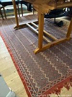 Overall shot of rug under wooden dining table showing pattern and red border