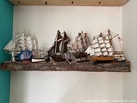 Five wood model ships displayed on a wooden shelf showing detail of sails, rigging, and flags, mostly white and brown colors