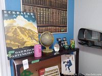 Photo showing mounted poster, globe, pink candle, art glass paperweight, and part of the metal whale shelf mounted on wall.