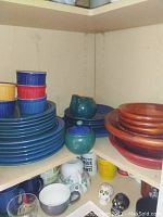 Blue ceramic plates and bowls stacked with darker green ceramic pitcher and sugar bowl, wood salad bowls adjacent