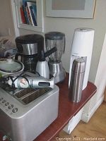 Overall lot view showing toaster, blender, Soda Stream, thermos and seltzer bottle on wooden table.