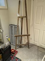 Full view of wooden easel standing against a wall with nearby items including a toolbox and heater.