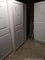 White cabinet with two paneled doors and silver curved handles in a basement setting