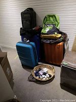 Overview of luggage and backpacks stacked near a wall with a basket of plugs in front.