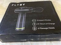 Black Flyby massage gun packaging box showing image of the device and specifications: 3 Impact Modes, 4+ Hours of Charge, 6 Massage Heads.