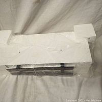 Photo of one white floating shelf packaged in plastic with foam padding on the ends for protection.