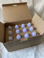 Opened box showing 12 white LED candle light bulbs with rounded flame tips inside a cardboard box labeled Lunasy LED Candle Light Bulb 6W