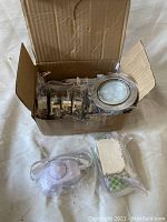 Open box showing round LED pot lights with metal rims, attached wiring, a white inline dimmer switch, and a power supply unit wrapped in plastic.