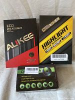 Three boxed car accessories: two LED headlight sets from ALIKEE and Carrover, and a car camera unit with specs on the box.