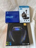 Three Bluetooth headphone boxes on white fabric background - Axloie wired earbuds, Soundcore Liberty Neo wireless earbuds, Legato Arc neckband headphones.