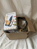 Photo of opened cardboard box showing the boxed 5-in-1 vegetable chopper and partially visible steam kettle wrapped in plastic