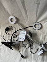 Two white ring LED makeup lights with clip-on stands and USB cables on gray fabric surface.
