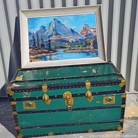 Green steamer trunk with brass latches and worn paint with mountain painting on top