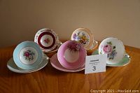 Front view of five teacup and saucer sets in pastel colors with floral designs and gold trim