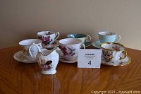 Overview photo showing the 6 teacups with saucers and one creamer, all vintage bone china with floral patterns and gold trim.