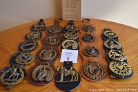 Five leather strips each with multiple brass horse brasses and a single horse brass on the right, along with a vintage booklet at the top back.