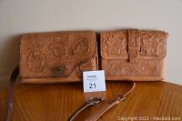 Two vintage hand tooled leather purses displayed front view on wood surface with straps detached on right side.