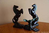 Two matching rearing horse figurines and one fawn figurine displayed on wood surface against a plain wall.