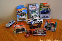 Overview of the lot showing multiple new and used diecast cars and vehicles in packaging and loose arranged on a wooden surface.
