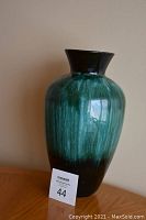 Full view of tall glazed pottery vase in green shades with dark top and bottom.