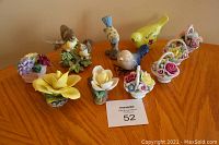 Full lot of 7 flower and 4 bird ceramic figurines displayed on wooden table.