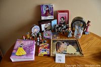 Full lot overview on table showing all 26 assorted Disney items including figures, photo album, tins, glass, framed art, and UNO game
