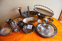 Overview of all tarnished silver plate items displayed on a wooden table including trays, bowls, goblets, salt & pepper shakers, basket, tongs, and plates.