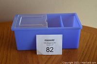 Blue plastic storage bin with three compartments and hinged clear lid on wooden surface with auction lot card