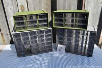 Four small parts storage containers displayed outside on a table: two green nine-drawer units on top, two grey thirty-drawer units on the bottom, one grey missing some drawers.