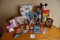 Photo showing full assortment on wooden table including the tablecloth package, paper plates, picture frames, tins, Pez dispenser, small figurines, and bookmarks.