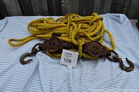 Photo showing entire hoist laid out with coiled yellow rope and two metal hoisting blocks with hooks, on a white and blue striped cloth.