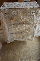 White lace tablecloth draped over a piece of furniture, showing the detailed lace pattern and overall size.