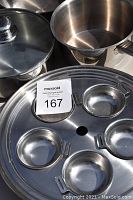 Close-up of the four-section pan, pot with lid and handle, and other pots showing stainless steel material and wear.