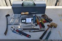 Photo showing the gray metal toolbox placed behind the assorted hand tools including screwdrivers, hammers, staple gun, safety glasses, adjustable wrench, and pry bar.