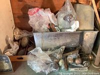 Wide view showing metal tray, plastic bags with items, and numerous door knobs of different styles and materials on and around the tray.