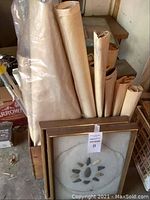 Two wooden frames containing assorted arrowheads arranged in a circular display, placed alongside a collection of rolled vintage posters and artwork.