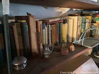Shelf with vintage hardcover books of various colors and sizes along with small silver colored decorative boxes and a miniature pitcher