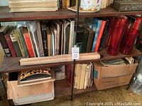 Shelves with mixed vintage books, rolled posters, red glass vases, and boxes underneath.