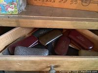 Drawer partially open showing numerous vintage glasses cases in various shades of brown and black leather or vinyl with gold embossed text.